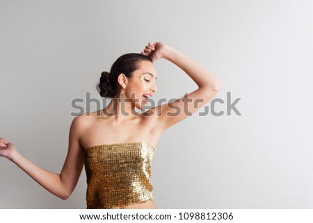 Portrait of beautiful ethnic indian young woman wearing sequins top in party, dancing with glitter make up on face, interior wall space. Fun female singing, glamour fashion model, cosmetics lifestyle.