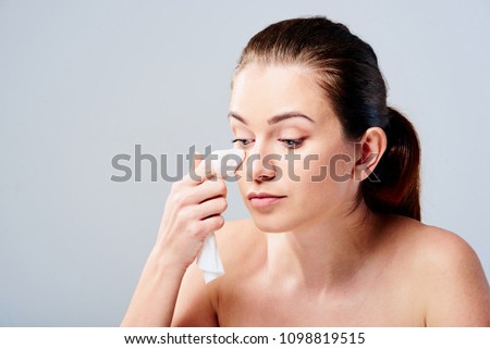 Portrait of a young brunette woman cleaning her face with wet wipes. Girl is removing make-up with facial tissues isolated on grey background. Beauty skin care concept. Royalty-Free Stock Photo #1098819515