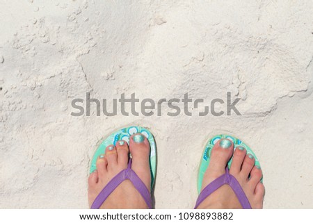Girl feet in blue slippers on sand beach texture. Tropical seashore. Seaside banner template with text place.  Summer vacation background. Coral beach sand texture. Smooth sunny sand beach
