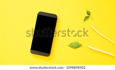 Workplace with smartphone and leaves on yellow background.(Top-view )