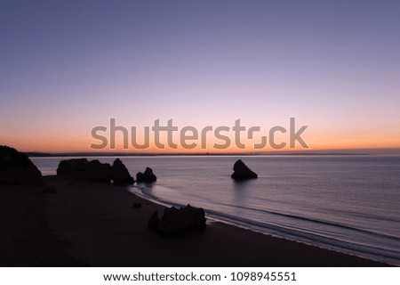 Sunrise over the ocean in Lagos, Portugal. Empty sandy beach with rock formations at sunrise.