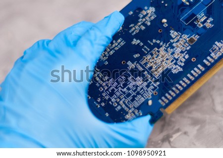 Mens hand in blue rubber glove holds PC graphics card with copper radiator on background of old scratched concrete floor
