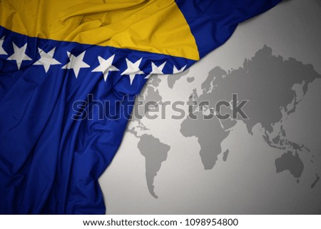 waving colorful national flag of bosnia and herzegovina on a gray world map background.