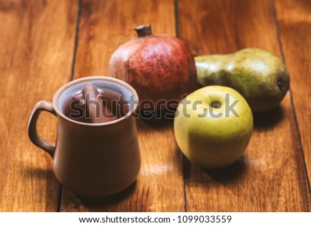 Clay cup with compote, pomegranate, apple, pear on a wooden table.