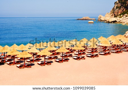Beach Umbrella made of palm leafs on the background of an exotic beach in Montenegro. Relaxing area: sun beds in the shadow of rustic umbrella. Sea view