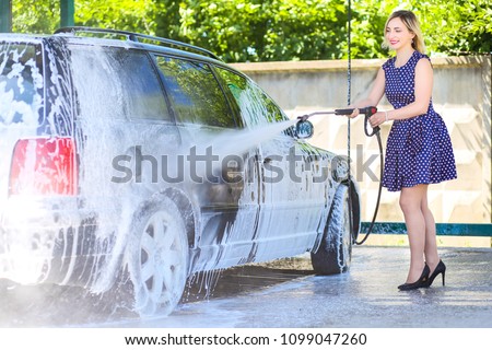 Picture, portrait of a young, smiling, attractive woman washing a car on a car wash, car wash, foam cleaning, pressure water