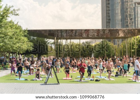 Blurred diverse group of people participating free public Yoga class at urban park with downtown buildings background. Outdoor Yoga training class on grass at summer day in Dallas, Texas, USA