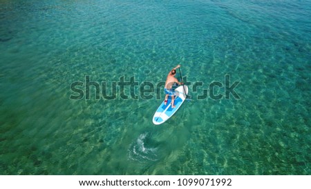 Aerial drone bird's eye view of man practicing sup or paddle surf boarding in tropical turquoise clear sea