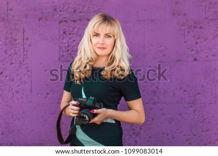 Portrait of beautiful young smiling blonde girl, female, woman, making photos at summer street. Portrait of professional photographer in casual\sports wear holding photo camera