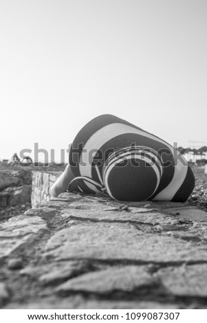 Greyscale image of a woman lying on a rocky promenade above a stony beach.