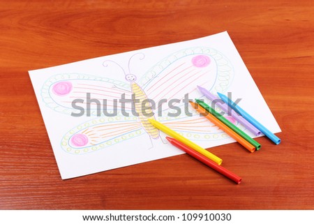 Children's drawing of butterfly and pencils on wooden background
