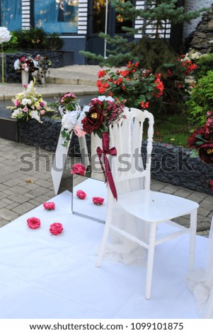 White vintage style chairs decorated with red / claret flowers: ranunculus and peony. Part of a wedding reception