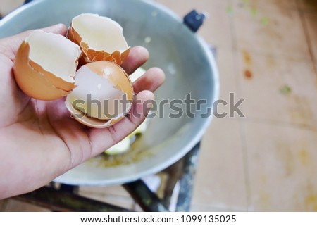 close up hand holding eggs shell.Fry pan fried omelette is background.
