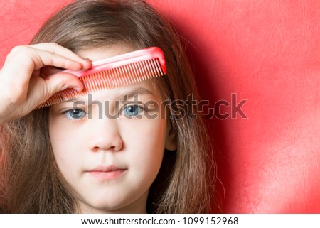 Cute little girl combs her eyebrows with a comb on a red background.