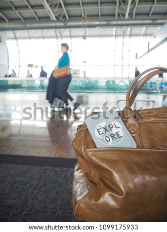 Bag and passport cover with motivational quote 'Explore' in a airport terminal with travelers in the background