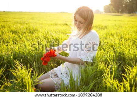 A girl sits on the green grass, and makes a wreath of red poppies