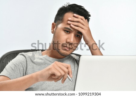Casually-dressed startup business man holding his head looking stressed while working on a laptop