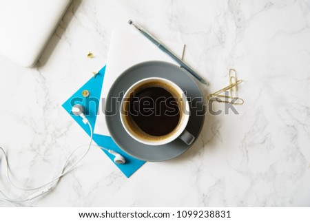 Workplace flatlay with notebook, blue card and coffee cup on marble table