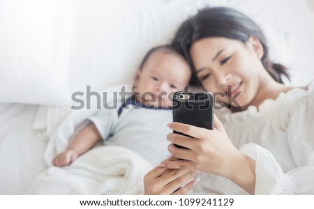Mother taking picture her newborn baby boy in bed with smart phone. Baby boy taking selfie with cell phone camera. Technology digital vlog communication with people concept