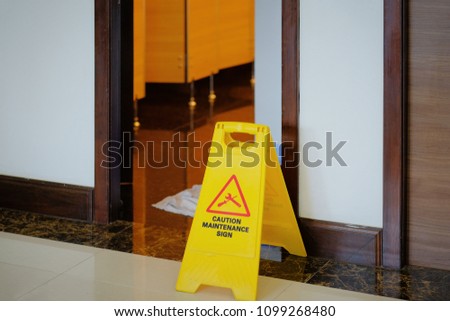 Yellow and red maintenance in progress warning sign in front of open door into a bathroom restroom with vintage traditional wooden door