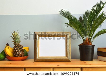 Summer tropical interior concept, frame with a blank space standing on an ald-school designed chest of drawers decorated with tropical palm in a pot and tropical fruits in a dish 