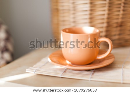 orange cup on wooden table with wicker napkin with light of sun