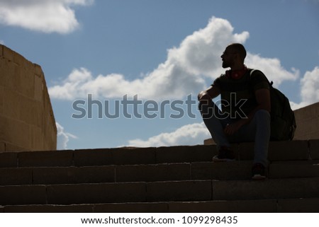 Down shot of a handsome young man wearing a casual outfit, sitting on the stairs and looking away.