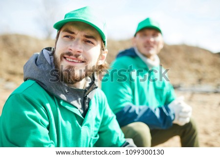 Bearded guy in green uniform and his colleague having rest after work in natural environment Royalty-Free Stock Photo #1099300130