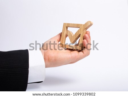 A man who is unemployed in a business suit is holding a wooden box. a tick in the box. The hand holds a wooden check box with a tick. Concept business goals and achievements. Performing tasks