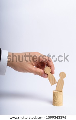 The man's hand of a businessman in a business suit holds a wooden figure of a man in his hand and moves another figure from his post. The concept of firing an employee, the replacement of staff