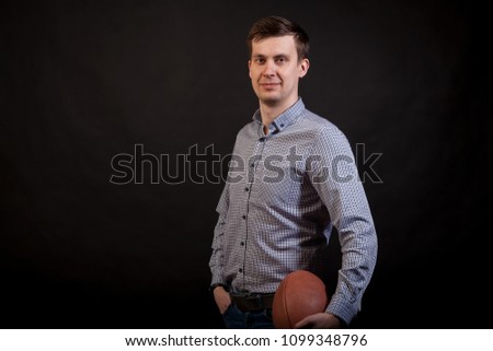 Dark-haired man in a plaid shirt 
holds a rugby ball in his hands on black isolated background