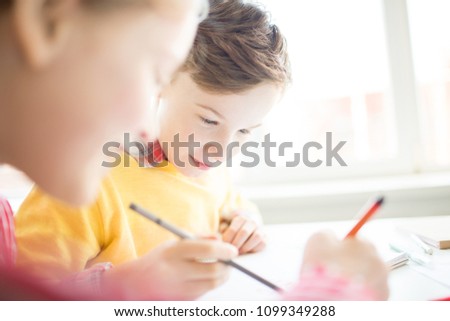 Cute youngster looking at picture on page of copybook of his classmate and discussing it