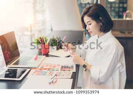 Young woman designer choosing colored pencils and color samples sheets for selection on office desk.