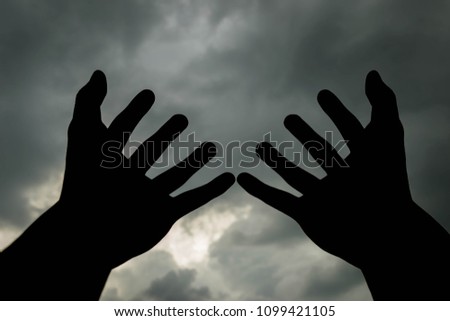 Raising two hands to the cloudy sky for helping in silhouette