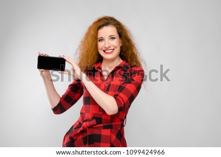 Young red-haired girl in a red checkered shirt. Young girl holding a phone