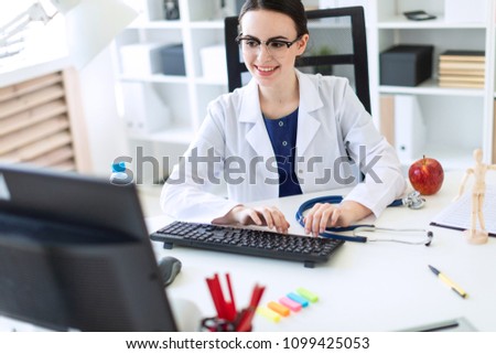 A beautiful young girl in a white robe is sitting at the table and typing on the keyboard.