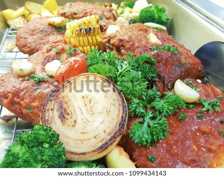 Closed up picture of roasted meat with sauce, onion, corn, garlic, vegetable and tomato