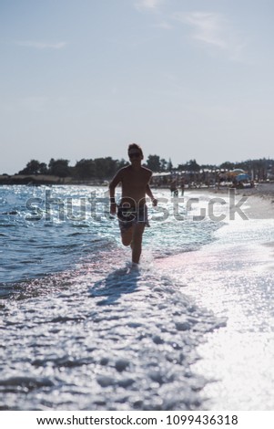 Happy kid running in the shallow water on the beach on a sunny day