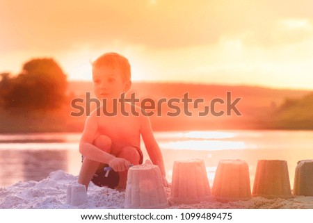 Little boy builds figures of sand on the river bank at sunset of the day, hands make shapes from wet sand