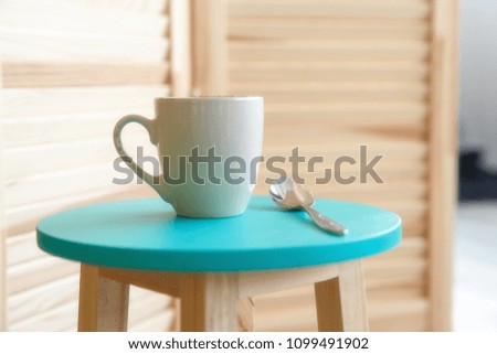 Cup of coffee in ceramic light cup on the turquoise stool in he room. Concept of light and happy morning in the hotel with taste coffee or tea.