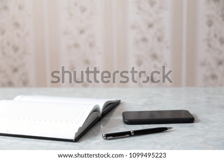 A blank notepad, pen and a smartphone on a grey table