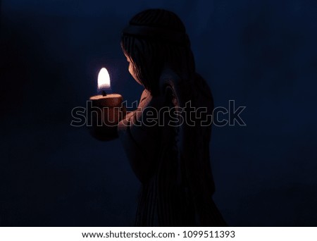 angel holds a burning candle in the dark. background religion, prayer and faith.