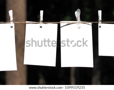 Empty paper sheet frames hanged by colored clothespins on dark nature  background. Blank cards on rope. Mock up for display of design, memo or congratulations backdrop. Pieces of paper, posters