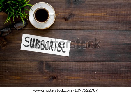 Email subscribe concept. Hand lettering subcribe on work desk with plant and cup of coffee on dark wooden background top view copy space