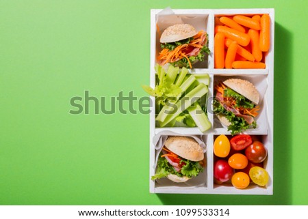 Homemade small burgers with ham, tomato, carrot, fresh salad served in old white wooben box on green background. Healthy junk food concept with copy space.