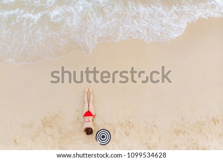 Top view Young woman in a red bikini lying and relaxing on the white sandy beach with turquoise sea water of thailand,aerial view from drone camera/ Summer concept.