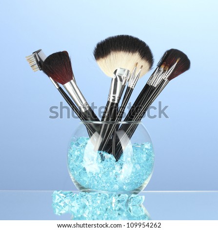 Make-up brushes in a bowl with stones on blue background