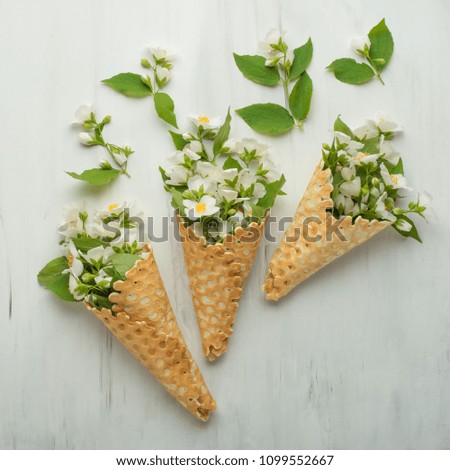 Flat spoons sweet cone waffle with white flowers on a light background background, top view. The concept of spring or summer mood