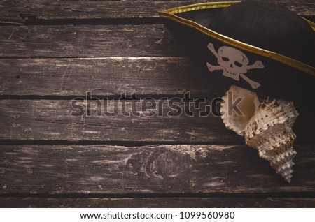 Pirate captain table concept background with copy space. Pirate hat and seashall on old wooden board.