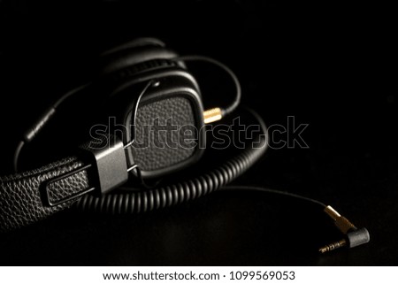 Black wired on ear headphones with gold headphone jack on dark background